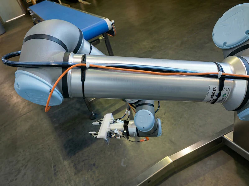 Flexroute TPV clamp guiding an orange pneumatic line along a metallic industrial robot arm.